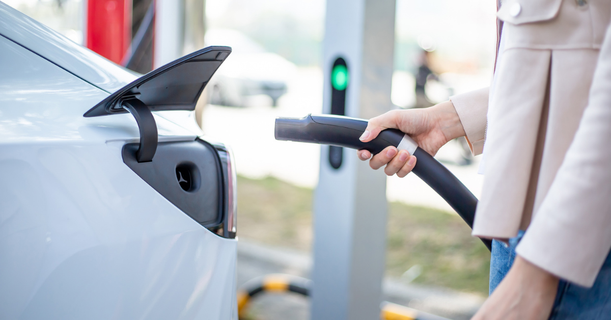 Asian woman plugging in electric charger into an electric car